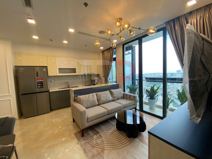 Phòng khách căn hộ hiện đại với sofa xám, bàn trà tròn đen và bếp liền kề nhìn ra ban công kính rộng