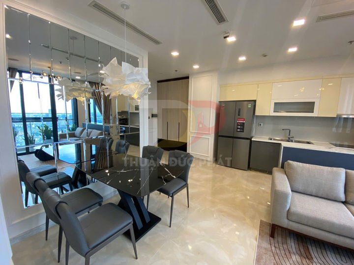 Bàn ăn mặt kính đen hiện đại trong căn hộ cao cấp liền kề bếp và phòng khách sáng rộng