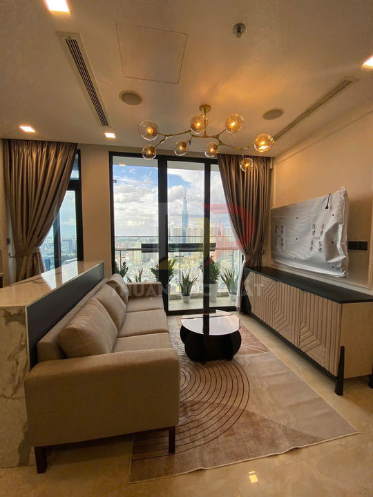 Phòng khách chung cư hiện đại với sofa vải màu be, bàn trà tròn, tủ kệ gỗ và cửa kính lớn nhìn ra thành phố