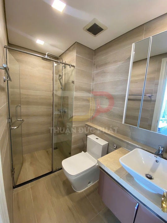 Phòng tắm hiện đại với buồng tắm kính, bồn cầu sứ trắng và lavabo đặt trên tủ gỗ