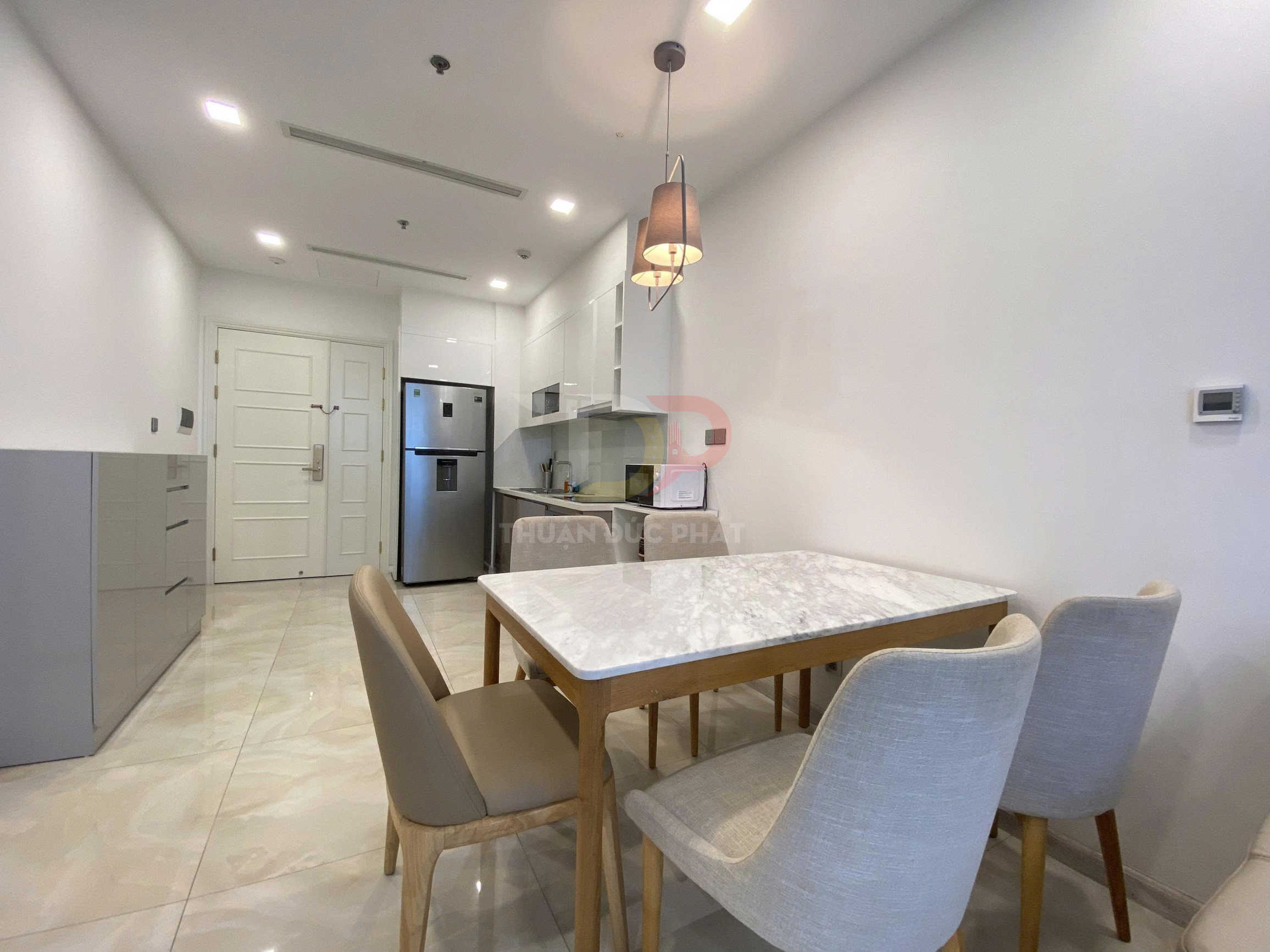 Bộ bàn ăn mặt đá với bốn ghế nệm trong căn bếp chung cư hiện đại, cạnh tủ lạnh inox