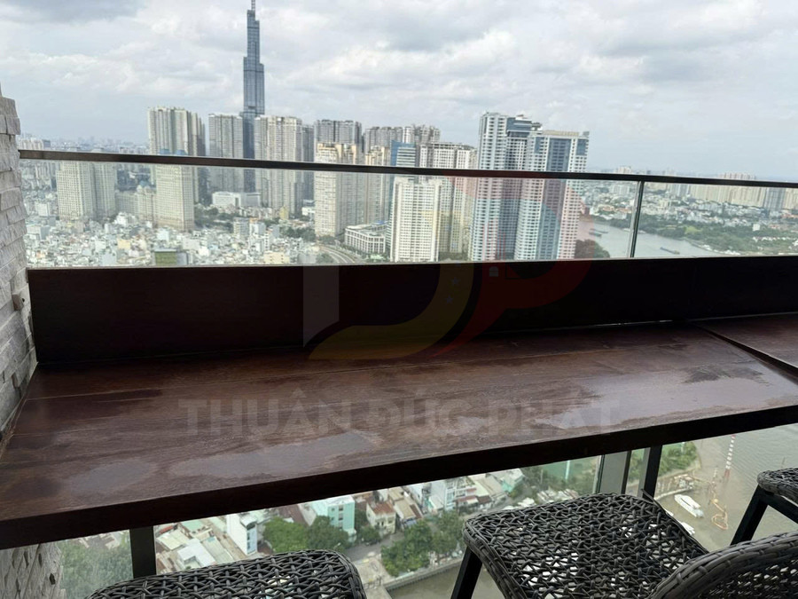 Bàn gỗ ngoài trời kèm ghế mây trên ban công kính, view toàn cảnh thành phố và sông