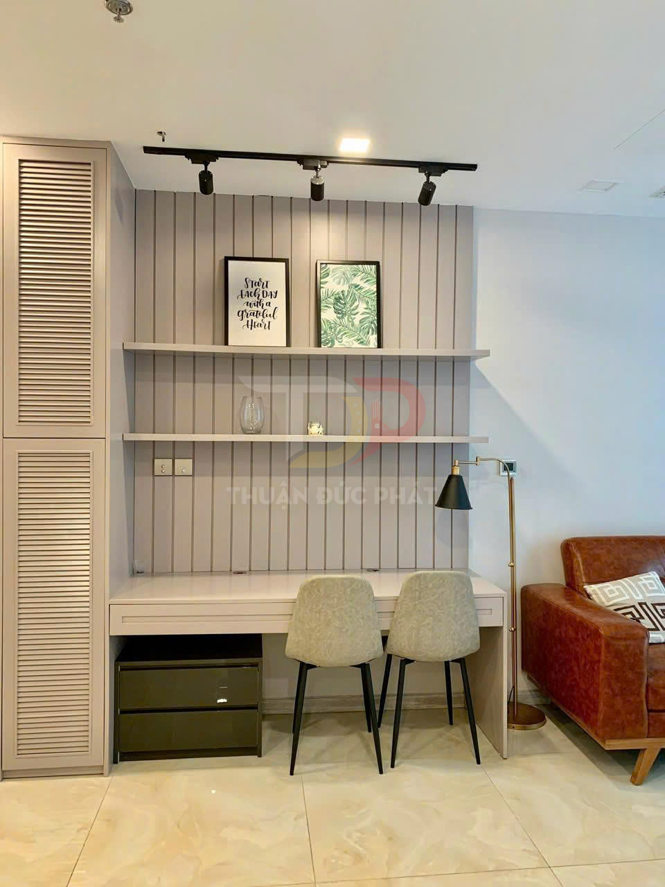 Bàn làm việc đôi hiện đại với hai ghế nệm, kệ treo tường trang trí tranh và đèn đọc sách cạnh sofa da