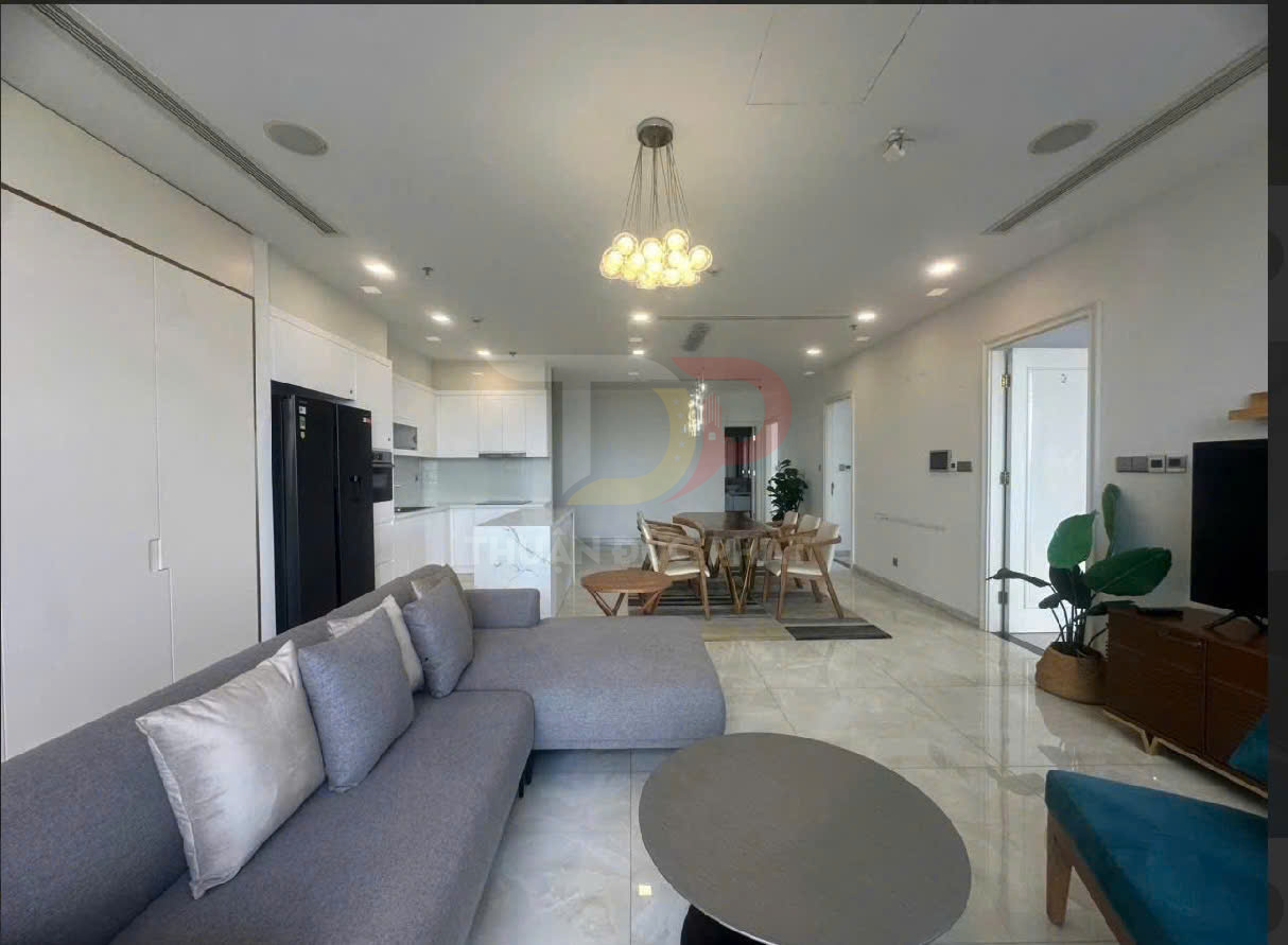 Phòng khách căn hộ hiện đại với sofa xám, bàn trà tròn, bếp mở và bộ bàn ăn gỗ sáng màu