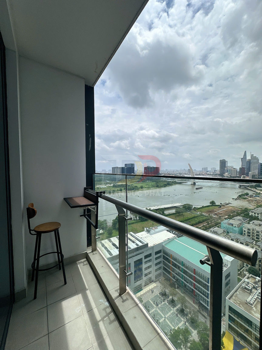 Ban công chung cư nhỏ với ghế bar và bàn gắn tường, lan can kính nhìn ra sông và thành phố