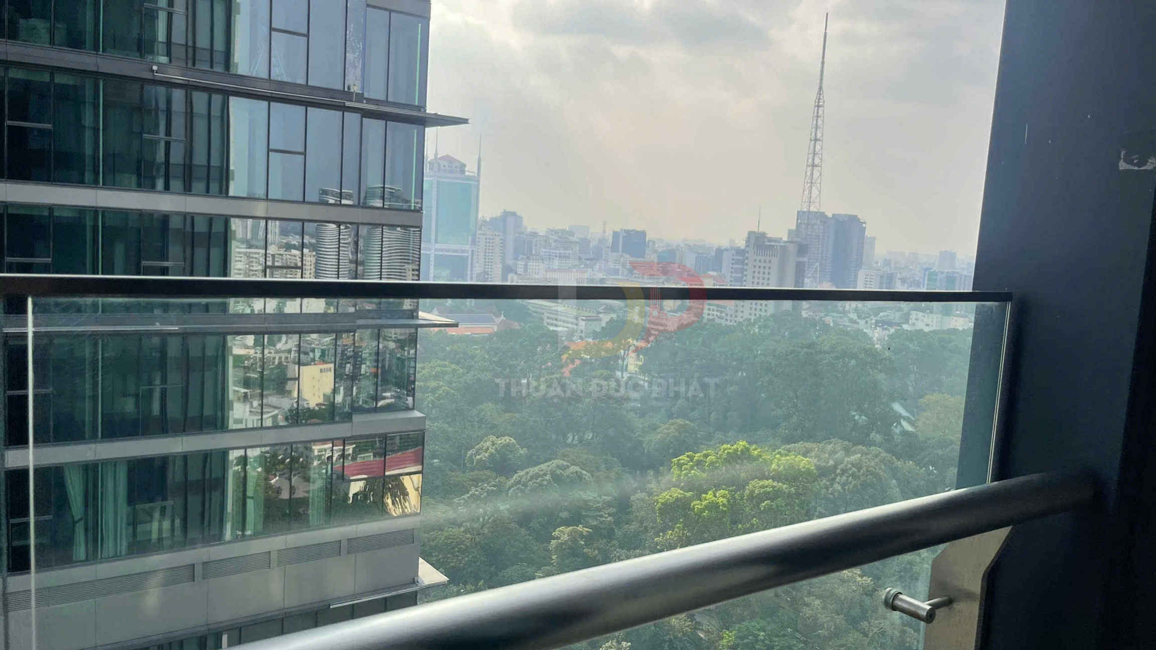 Lan can kính cường lực ban công chung cư nhìn ra tòa nhà văn phòng và công viên cây xanh