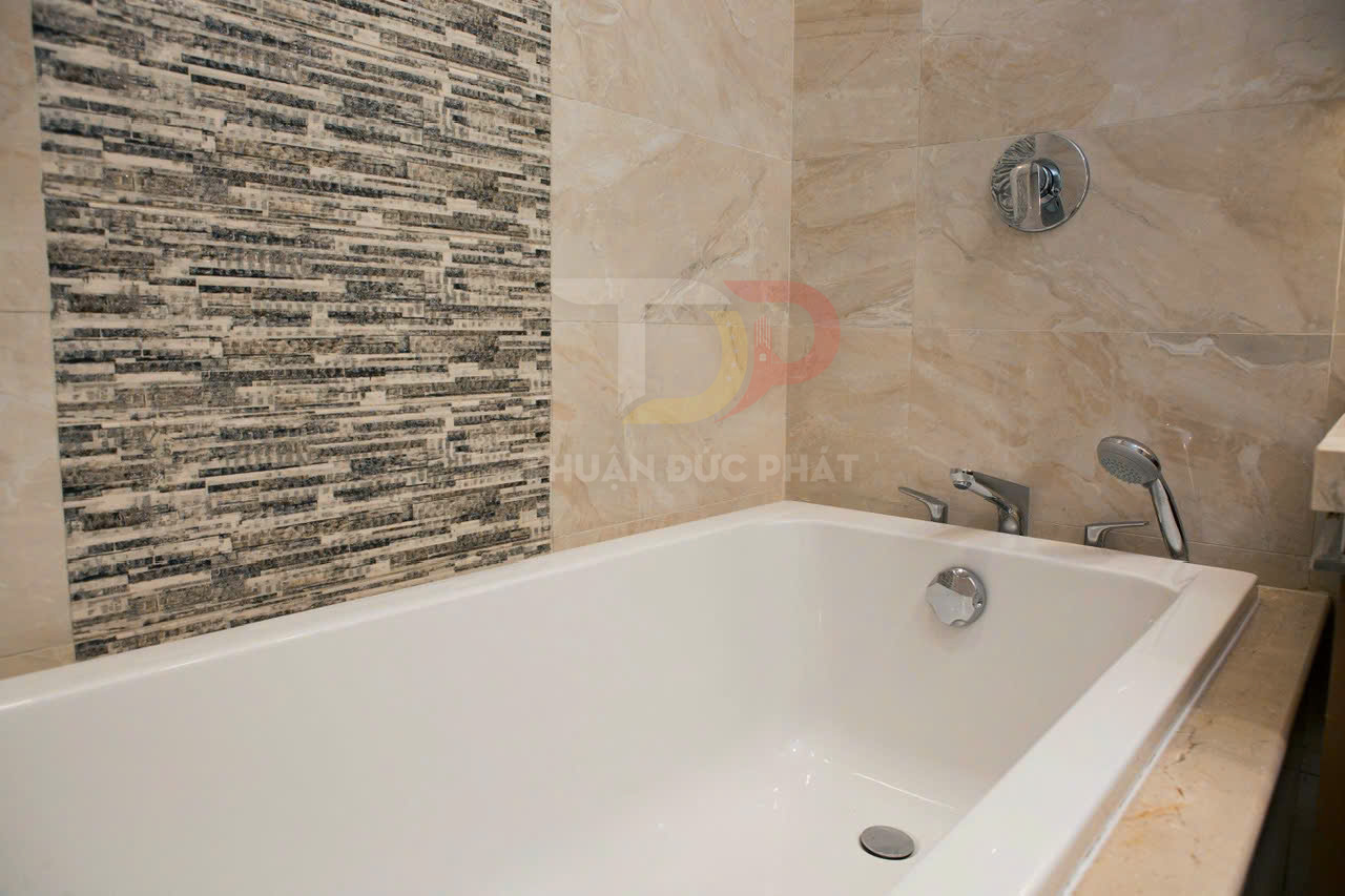 Bồn tắm nằm trắng với vòi sen tay và tường ốp gạch đá hoa văn hiện đại trong phòng tắm