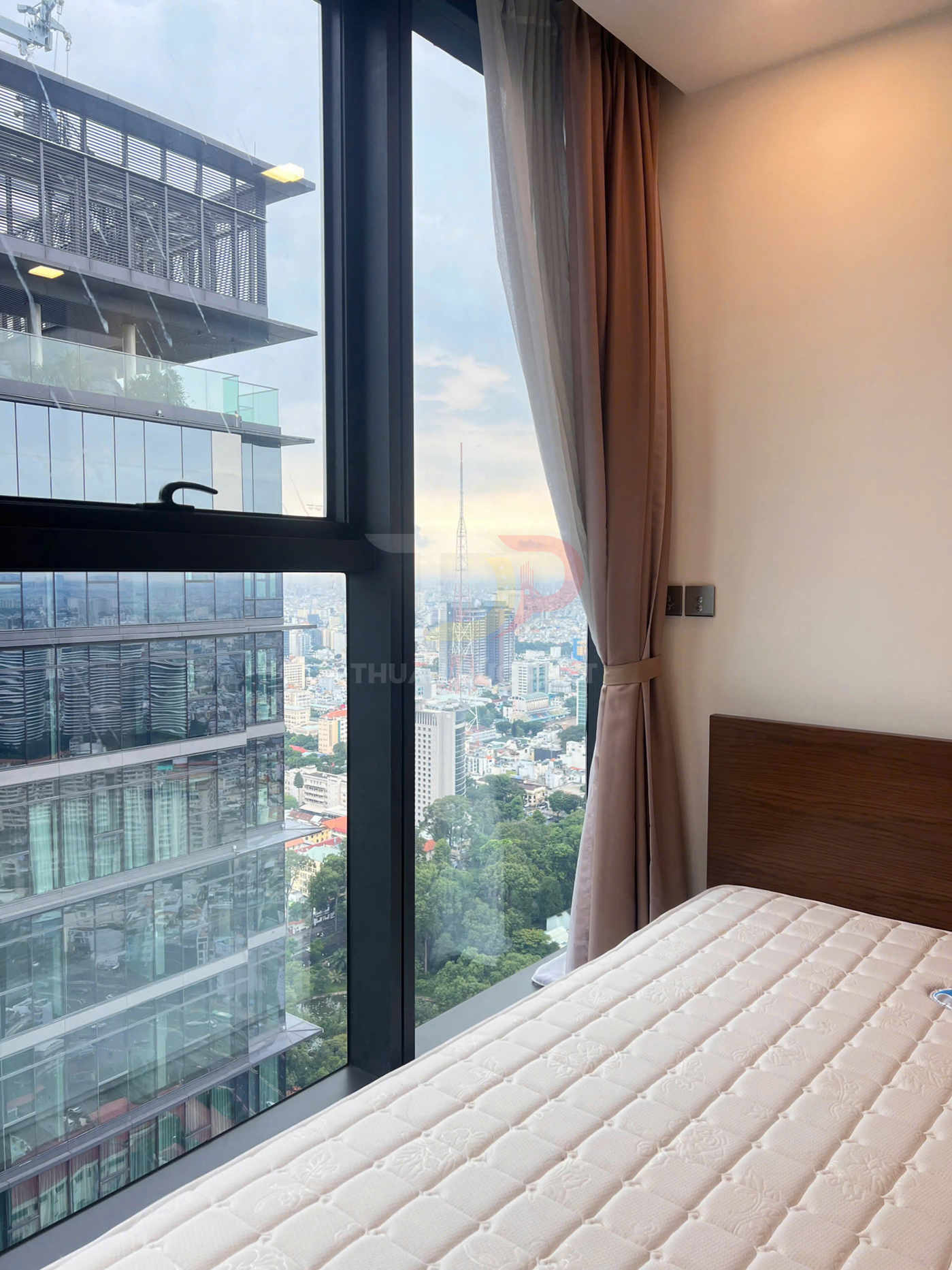 Giường ngủ với nệm trắng cạnh cửa sổ kính lớn, view thành phố và tòa nhà cao tầng hiện đại