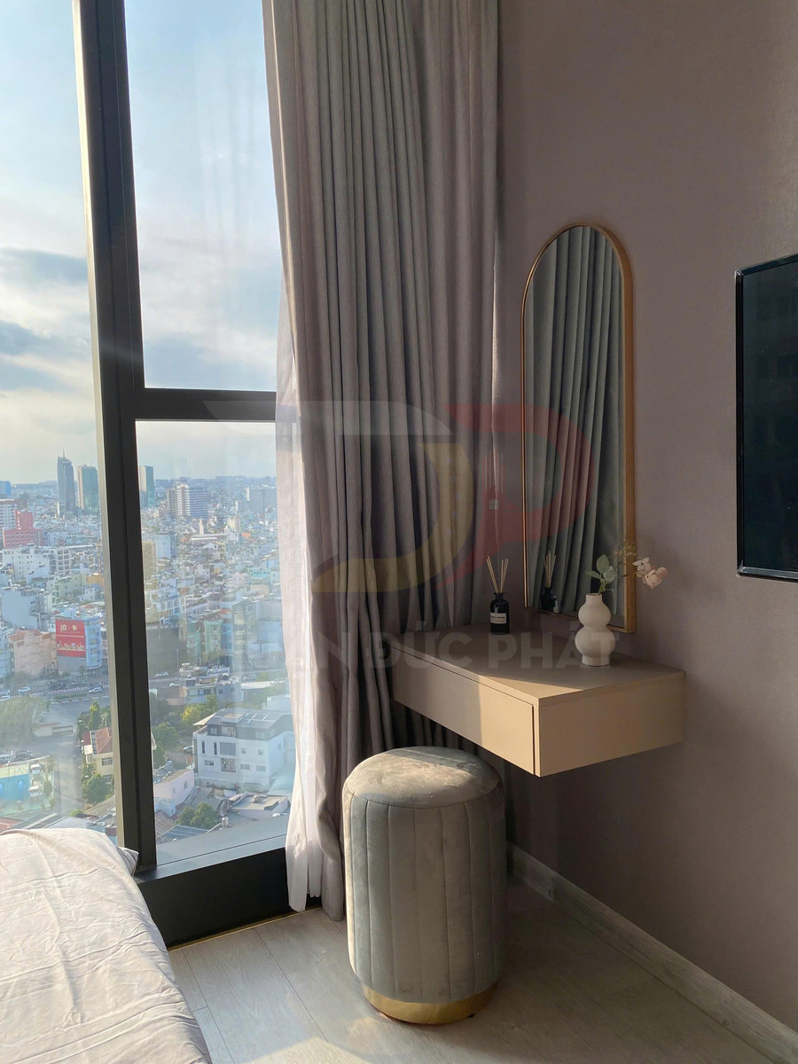Bàn trang điểm treo tường màu be với gương bo tròn và ghế đôn bọc nỉ trong phòng ngủ cạnh cửa sổ lớn