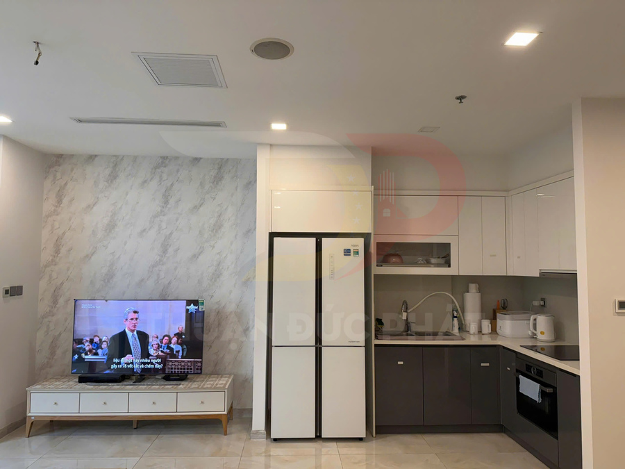 Phòng bếp hiện đại với tủ lạnh hai cánh màu trắng, tủ bếp chữ L và tivi đặt cạnh tường đá marble