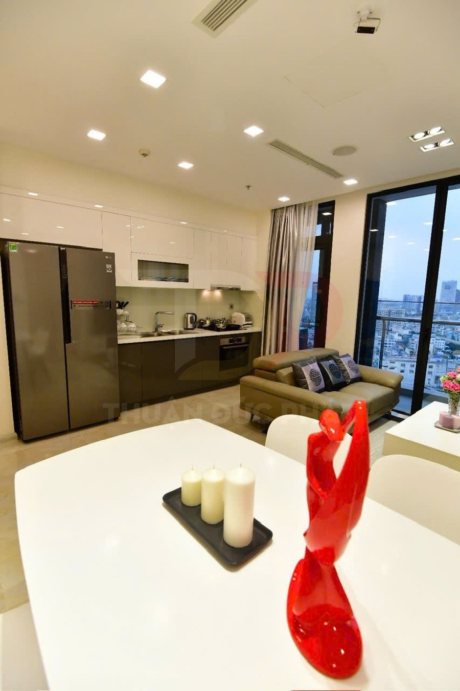 Căn hộ hiện đại với bếp liền phòng khách, bàn ăn trắng trang trí tượng đỏ và bộ sofa cạnh cửa kính lớn