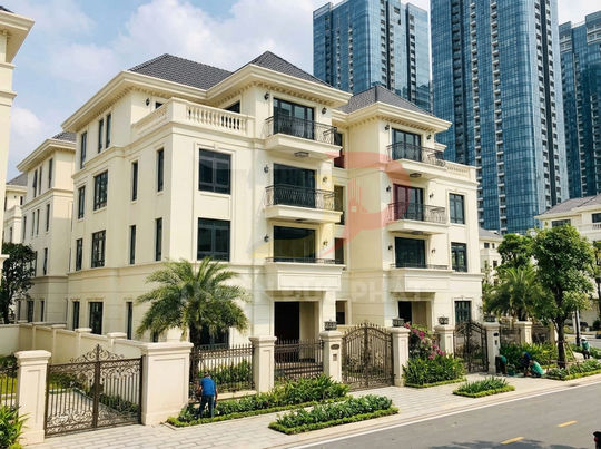 Biệt thự cao cấp 3 tầng màu trắng với sân vườn và hàng rào sắt, phía sau là các tòa chung cư cao tầng
