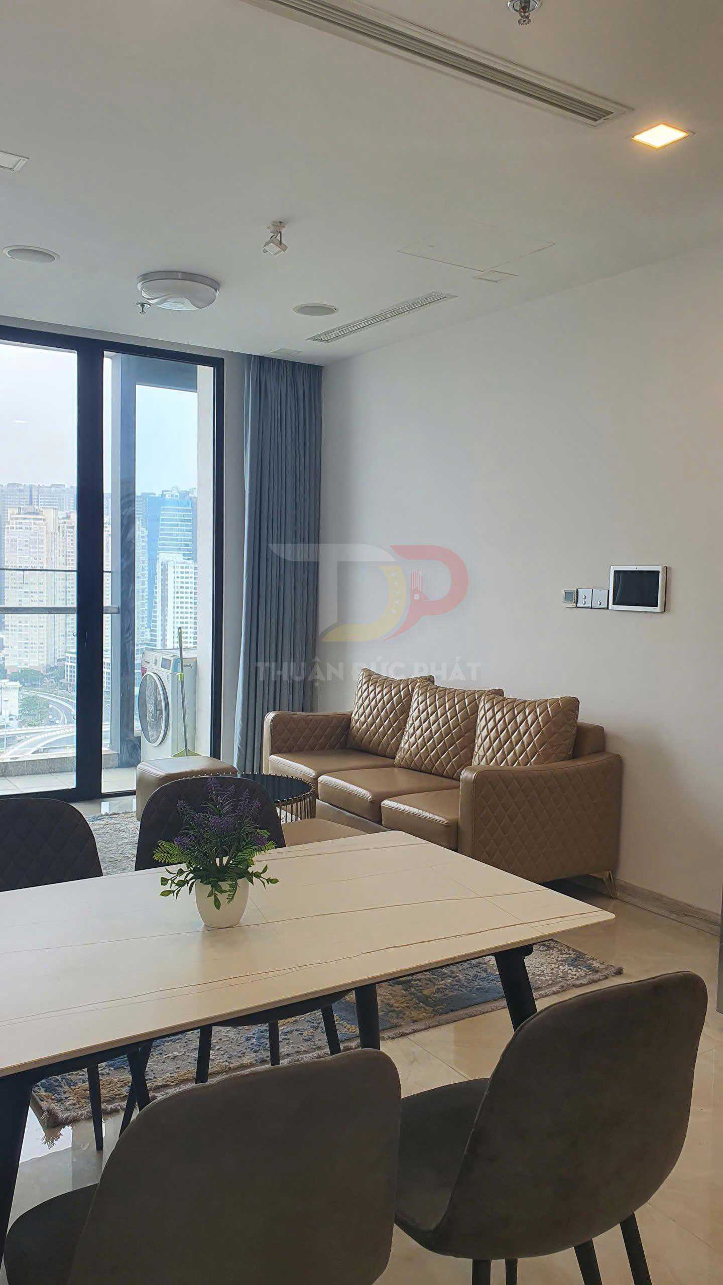 Phòng khách chung cư hiện đại với sofa da màu nâu, bàn ăn gỗ và cửa kính lớn nhìn ra ban công