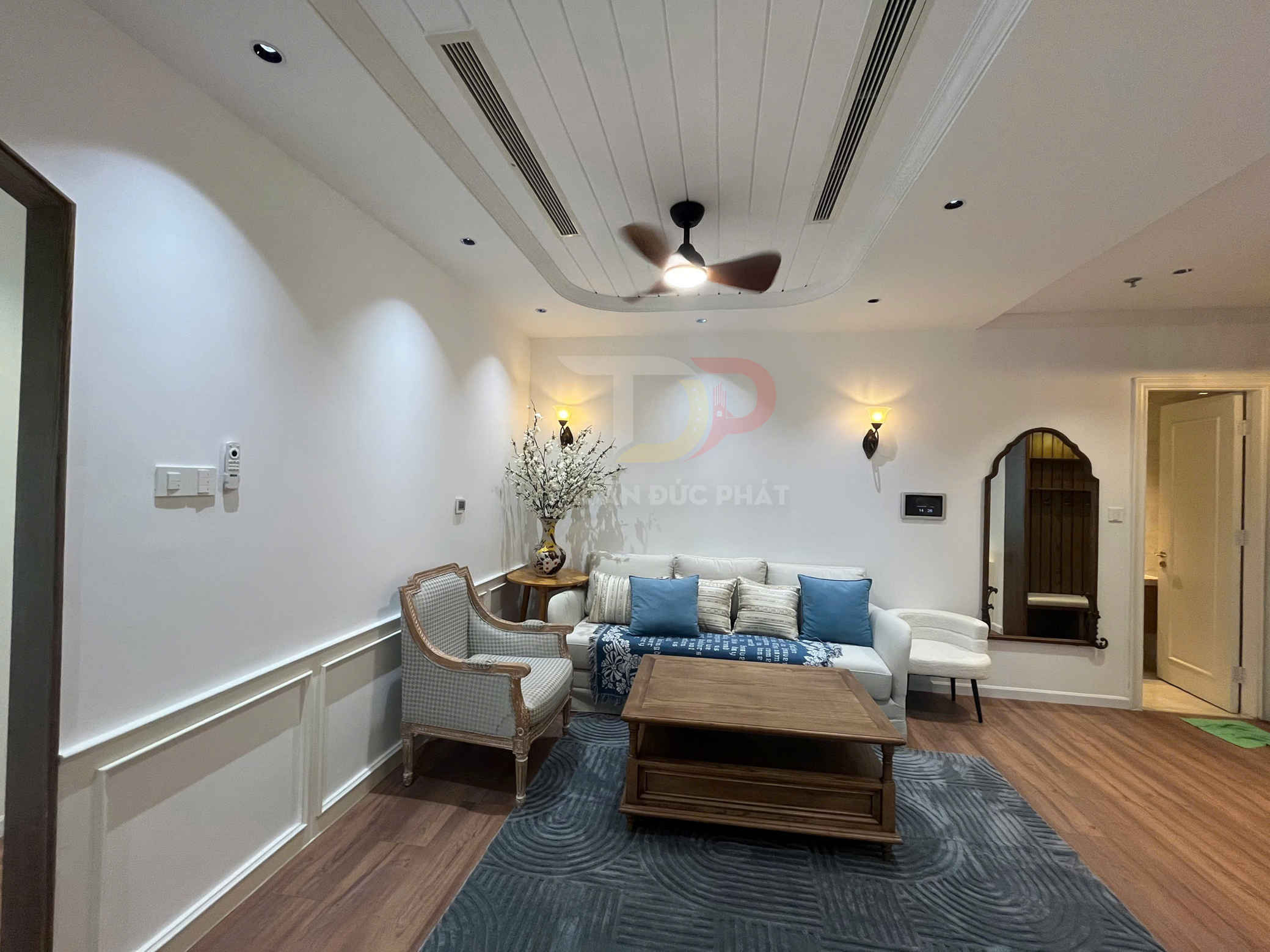 Phòng khách hiện đại với sofa trắng gối xanh, bàn trà gỗ và ghế bành cạnh bình hoa trang trí