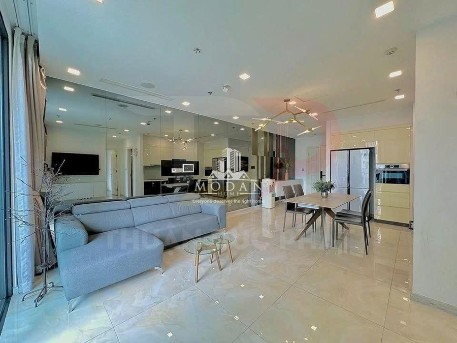 Phòng khách và bếp căn hộ hiện đại với sofa xám, bàn ăn gỗ, bếp âm tường và tủ lạnh lớn