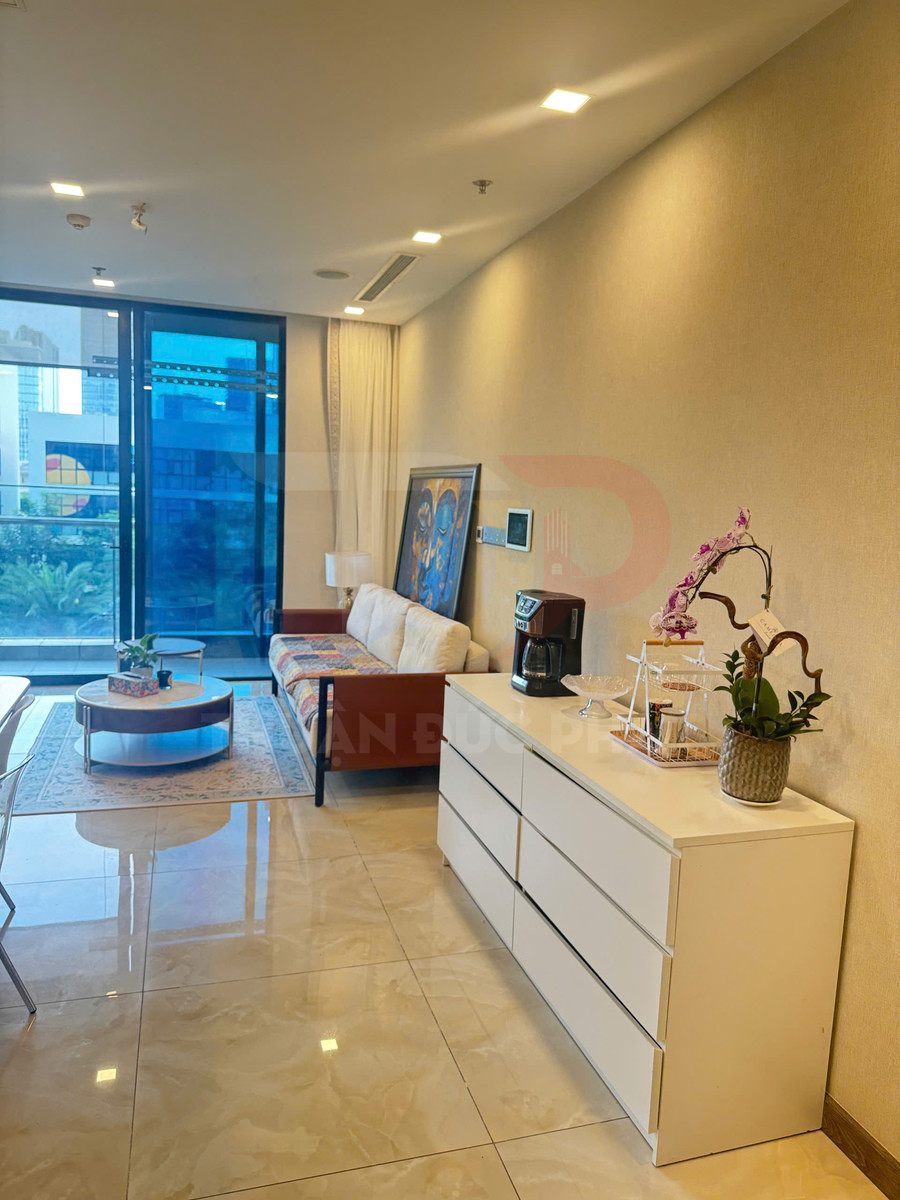 Phòng khách chung cư hiện đại với sofa, bàn trà tròn, tủ trắng đặt máy pha cà phê và chậu hoa lan
