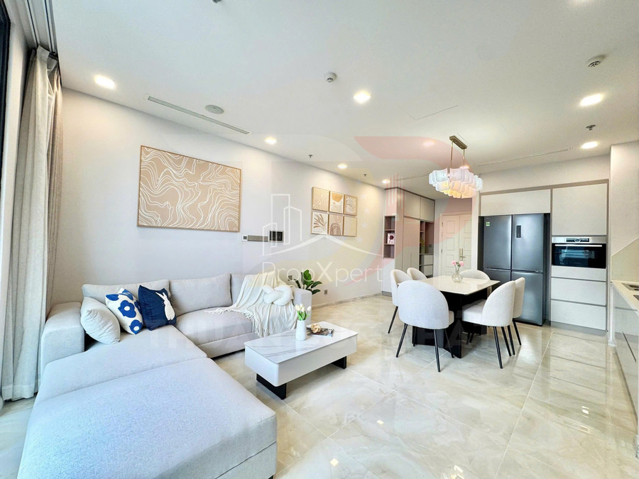 Phòng khách và bếp căn hộ hiện đại với sofa chữ L màu xám, bàn trà, bàn ăn và tủ bếp tone trắng sáng