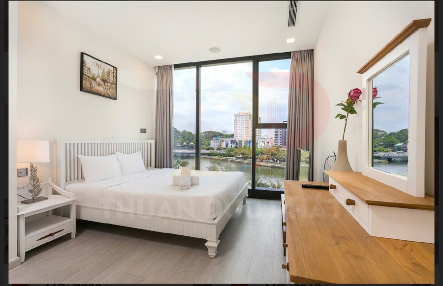 Phòng ngủ khách sạn giường đôi trắng, cửa kính lớn view sông và thành phố, nội thất gỗ hiện đại