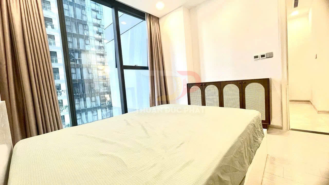 Phòng ngủ chung cư sáng với giường đôi, cửa sổ kính lớn và rèm nâu nhìn ra tòa nhà cao tầng