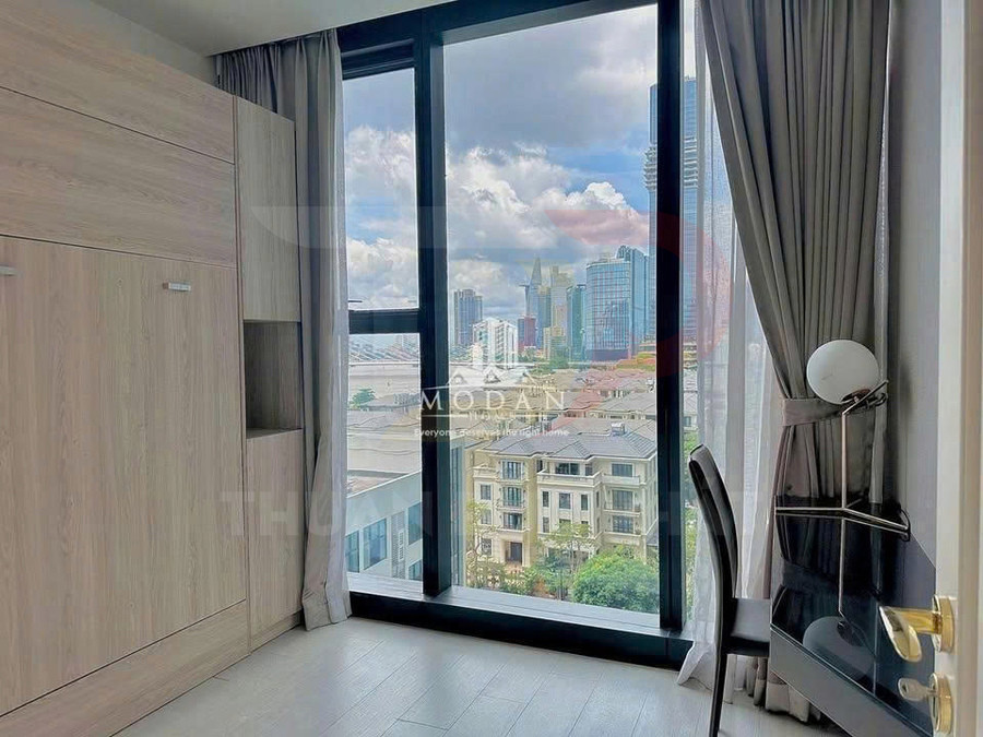 Căn hộ có cửa sổ kính lớn, nội thất gỗ sáng màu, bàn làm việc nhỏ nhìn ra view thành phố hiện đại