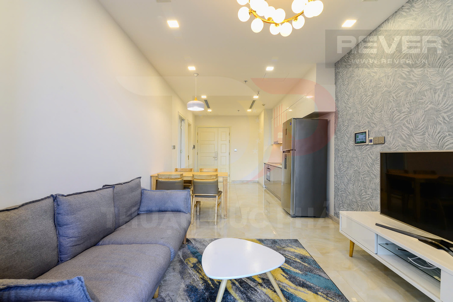Phòng khách căn hộ hiện đại với sofa xám, bàn trà trắng, tivi và bếp liền kề có tủ lạnh inox