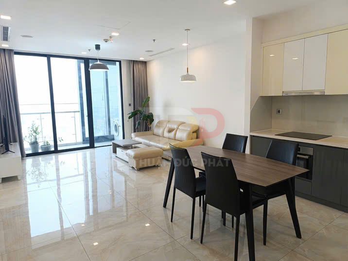 Phòng khách căn hộ hiện đại với sofa da màu kem, bàn ăn gỗ bốn ghế và bếp liền kề sáng thoáng