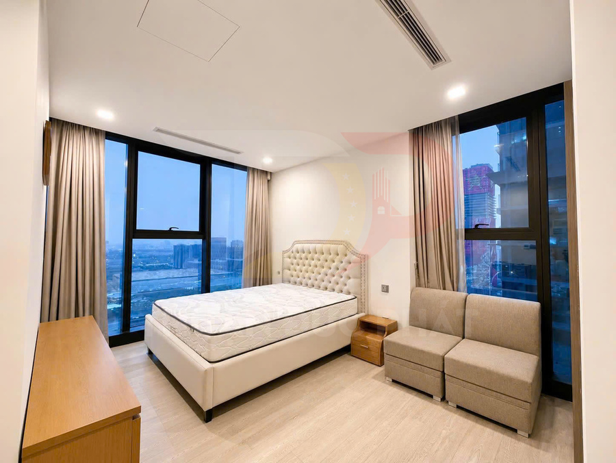 Phòng ngủ hiện đại với giường nệm lớn cạnh cửa sổ kính rộng và ghế sofa nhỏ màu be