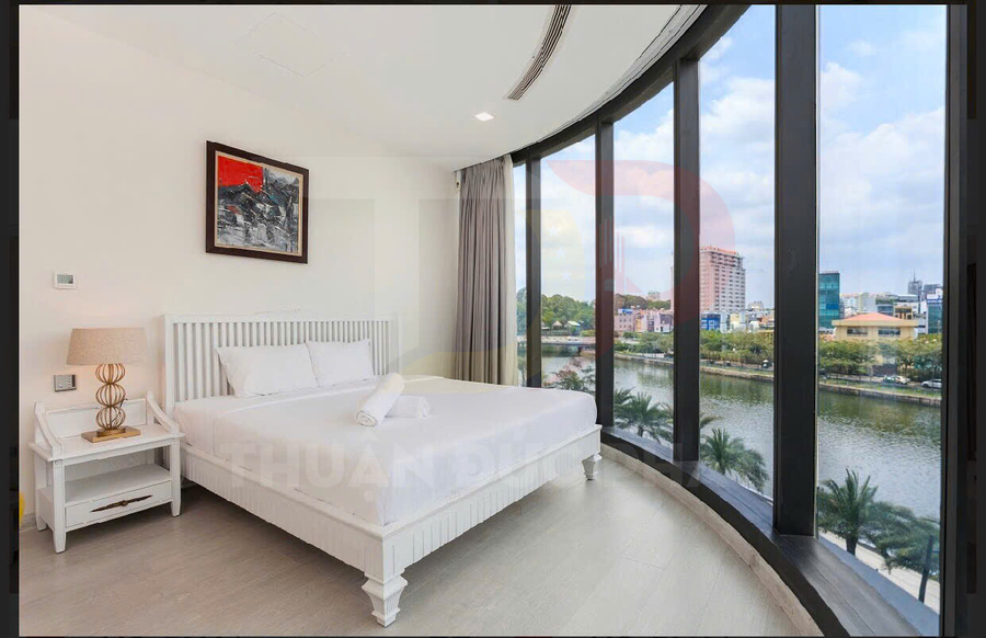 Phòng ngủ hiện đại với giường đôi trắng cạnh cửa sổ kính lớn nhìn ra sông và thành phố