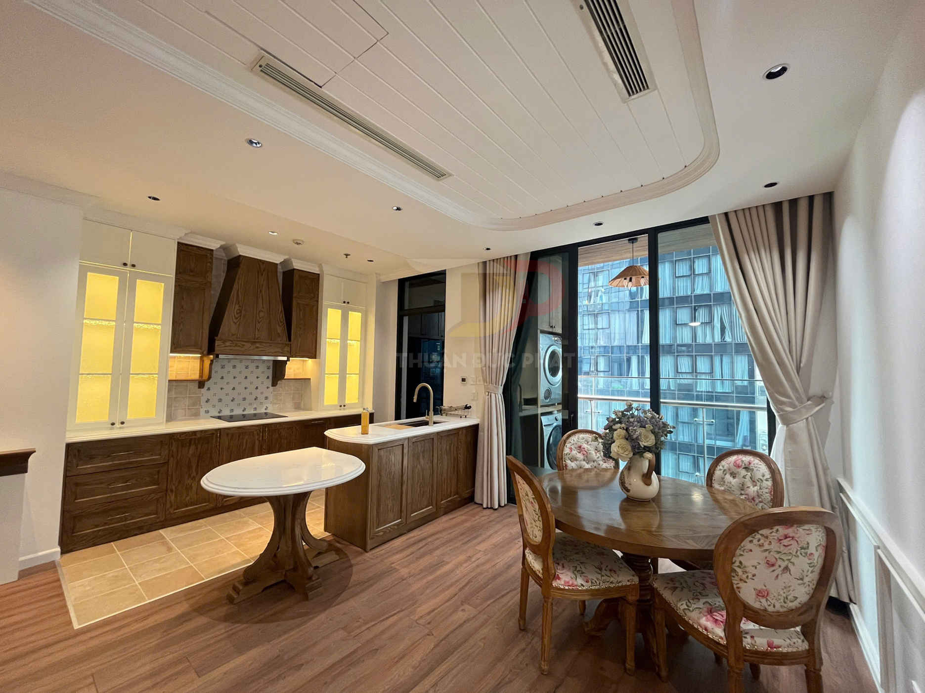 Phòng bếp và bàn ăn gỗ phong cách tân cổ điển với tủ bếp, đảo bếp và bộ ghế hoa cạnh cửa sổ lớn