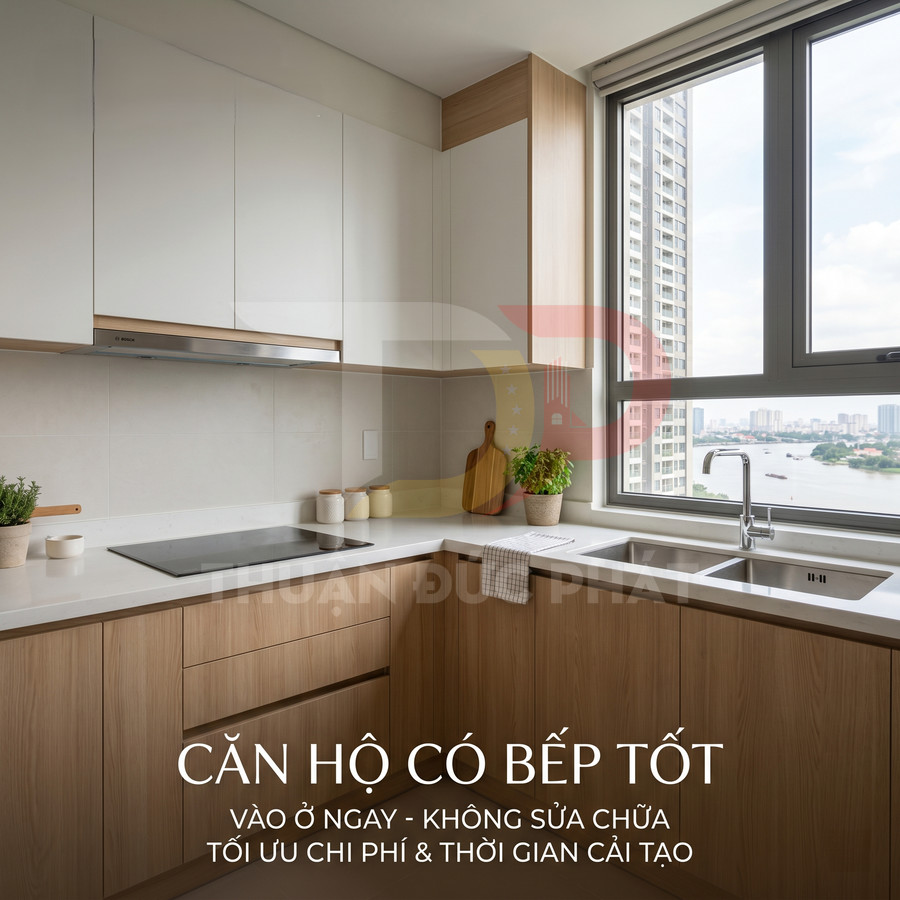 Căn hộ có bếp hiện đại, tủ gỗ, bếp từ, chậu rửa cạnh cửa sổ lớn nhìn ra sông và chung cư