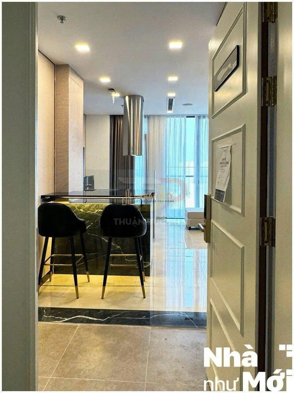 Căn hộ cao cấp với quầy bar đá đen, hai ghế cao và phòng khách sáng có cửa kính lớn