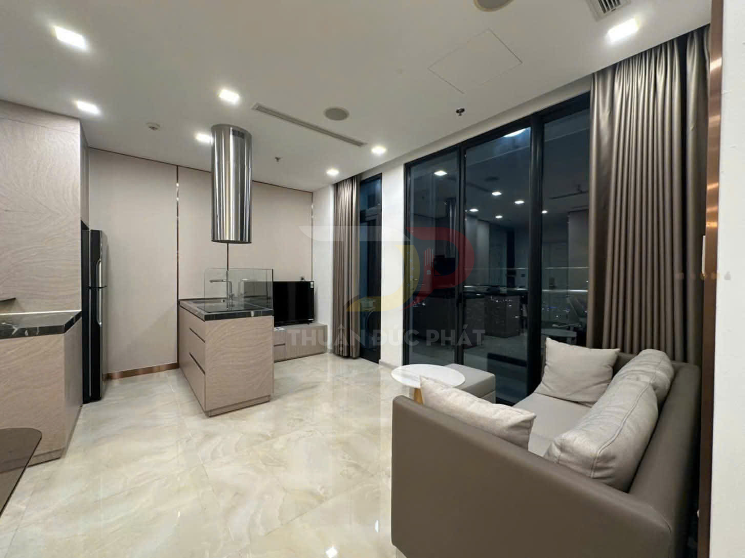 Phòng khách căn hộ hiện đại với sofa da màu be, bếp mở và cửa kính lớn nhìn ra ban công