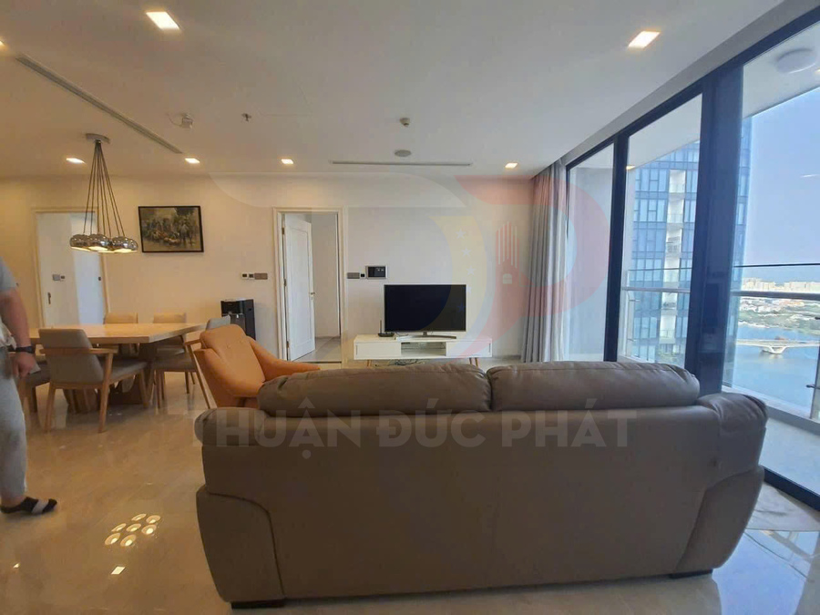 Phòng khách căn hộ hiện đại với sofa da, bàn ăn gỗ và cửa kính lớn nhìn ra view sông
