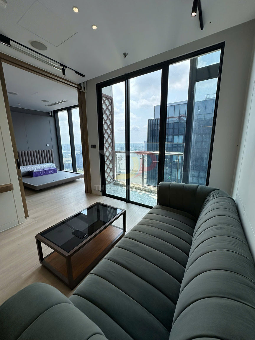 Sofa vải màu xanh đậm và bàn trà kính trong phòng khách căn hộ view cửa kính lớn ra thành phố