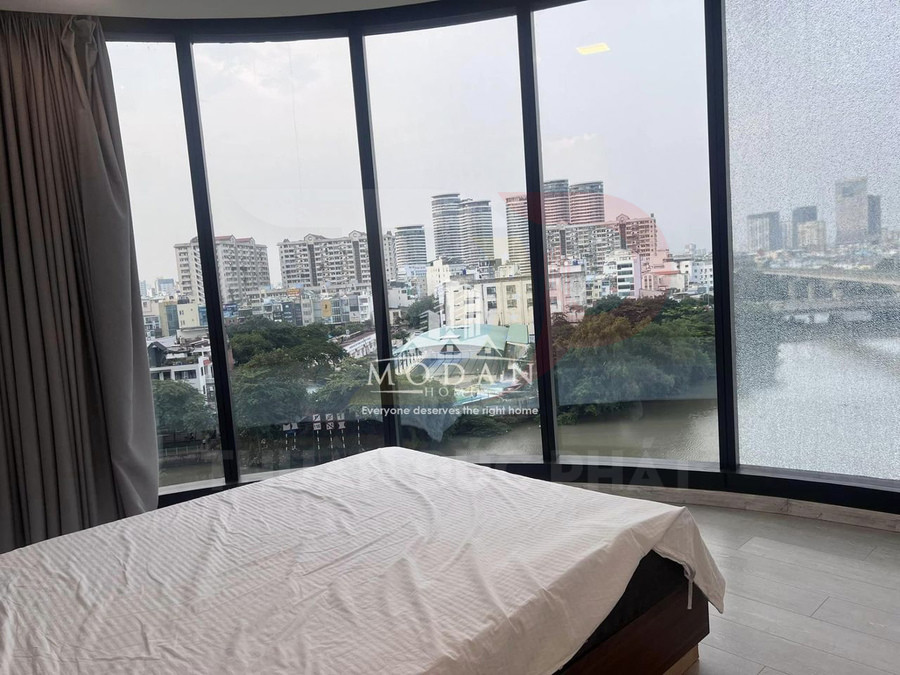 Phòng ngủ với giường đôi cạnh cửa kính lớn nhìn ra sông và khu chung cư cao tầng