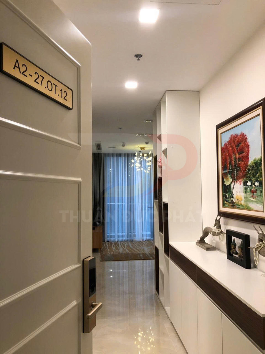 Cửa căn hộ A2 27.OT.12 mở vào hành lang nội thất hiện đại với tủ trang trí và tranh treo tường