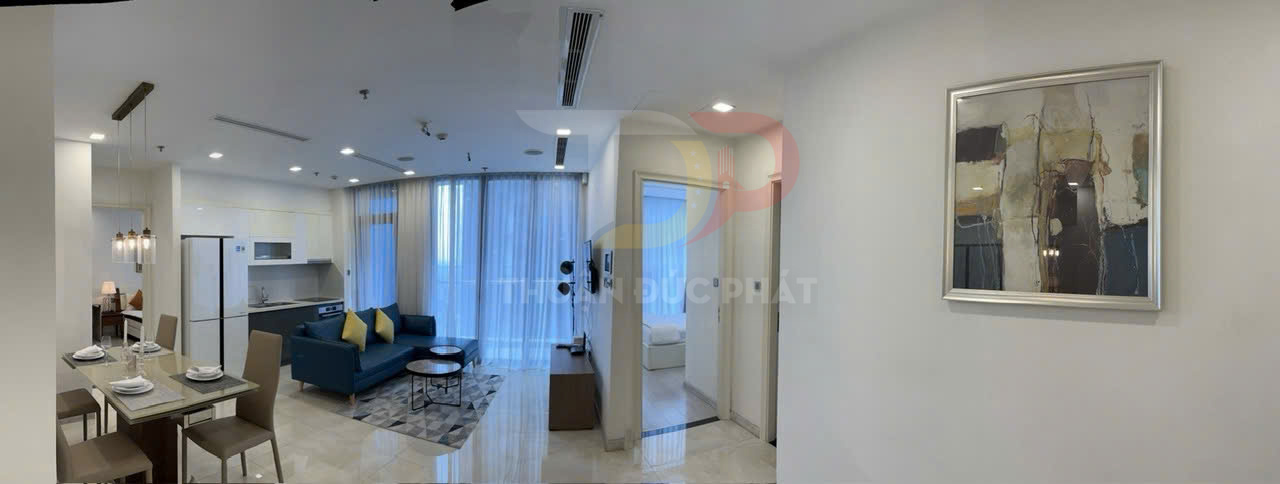 Căn hộ hiện đại với phòng khách liền bếp, sofa xanh, bàn ăn và cửa kính lớn đón ánh sáng tự nhiên