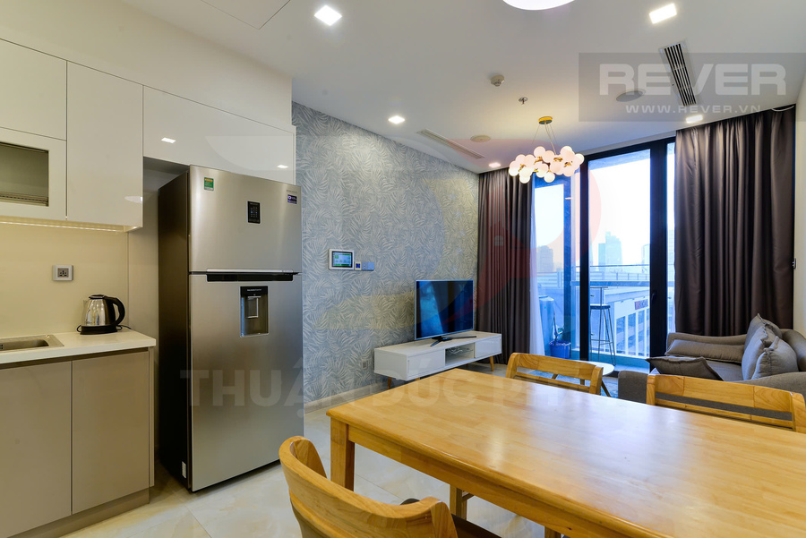 Căn hộ hiện đại với bếp, tủ lạnh inox, bàn ăn gỗ, sofa và tivi cạnh cửa kính lớn nhìn ra ban công