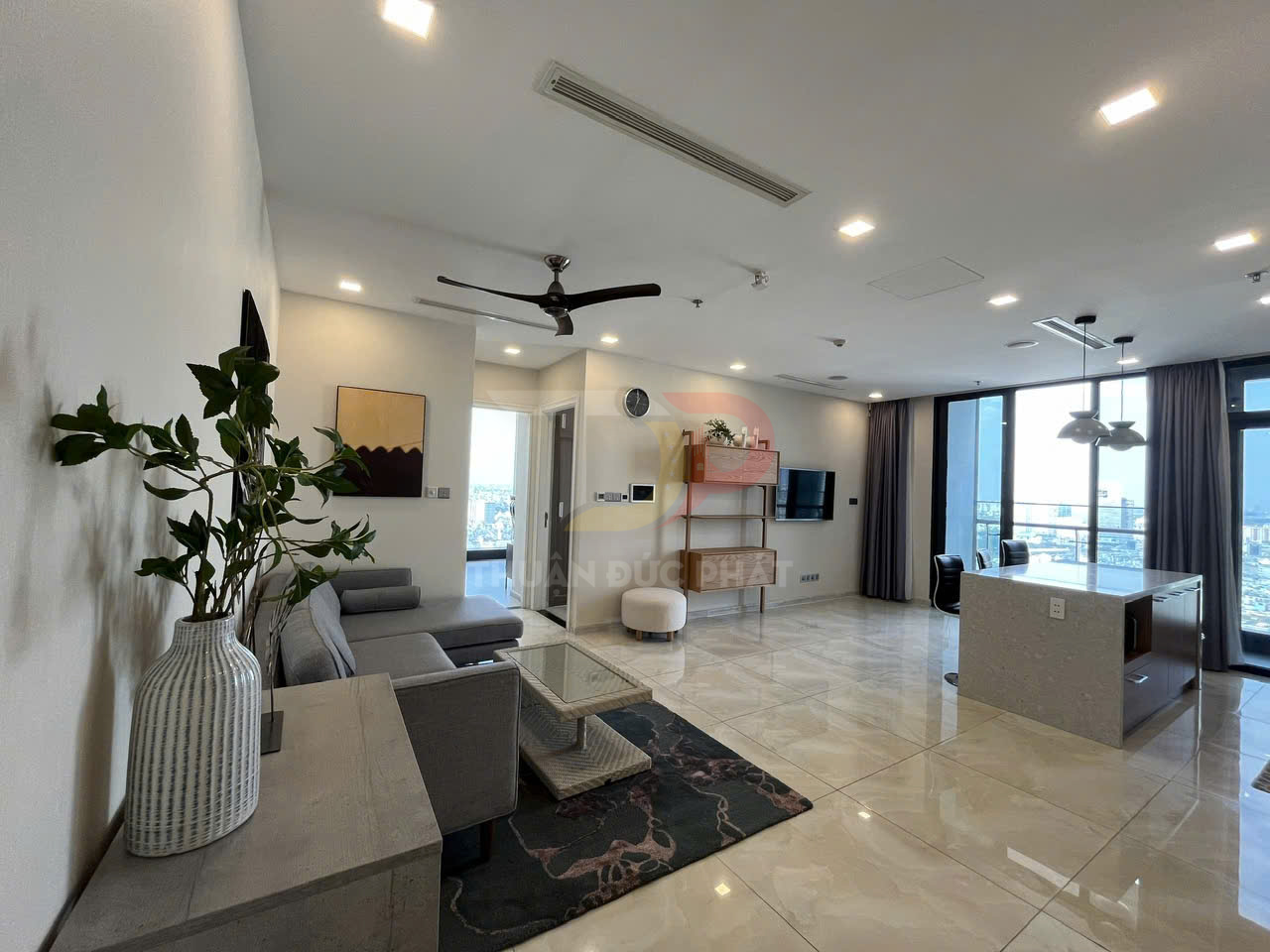 Phòng khách căn hộ cao cấp với sofa xám, bàn kính, bếp mở và cửa kính lớn nhìn ra thành phố