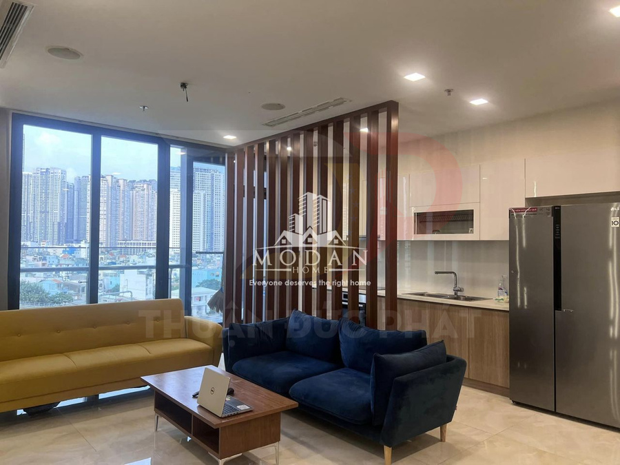 Phòng khách căn hộ hiện đại với sofa, bàn gỗ, bếp mở và tủ lạnh cạnh cửa sổ lớn view thành phố