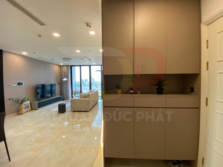 Phòng khách chung cư hiện đại với tủ giày âm tường, sofa sáng màu và kệ tivi treo tường cạnh cửa sổ lớn