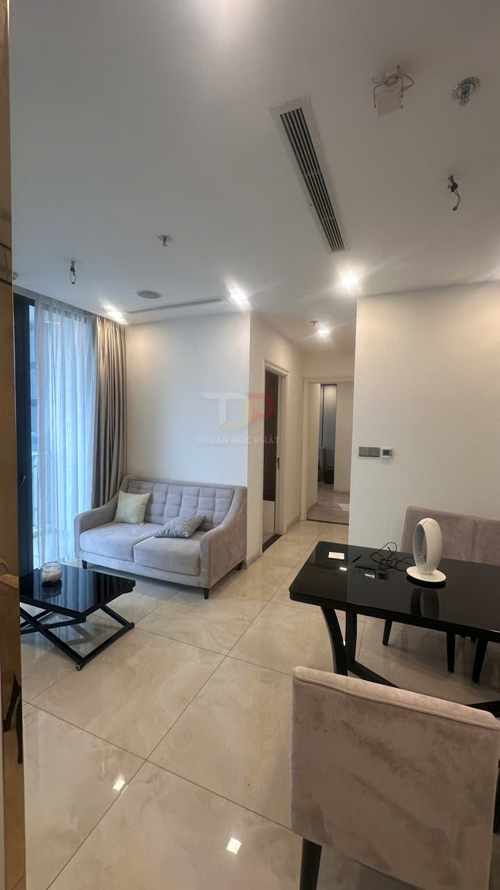 Phòng khách căn hộ hiện đại với sofa màu be, bàn trà kính đen và bàn ăn cạnh cửa sổ lớn có rèm trắng