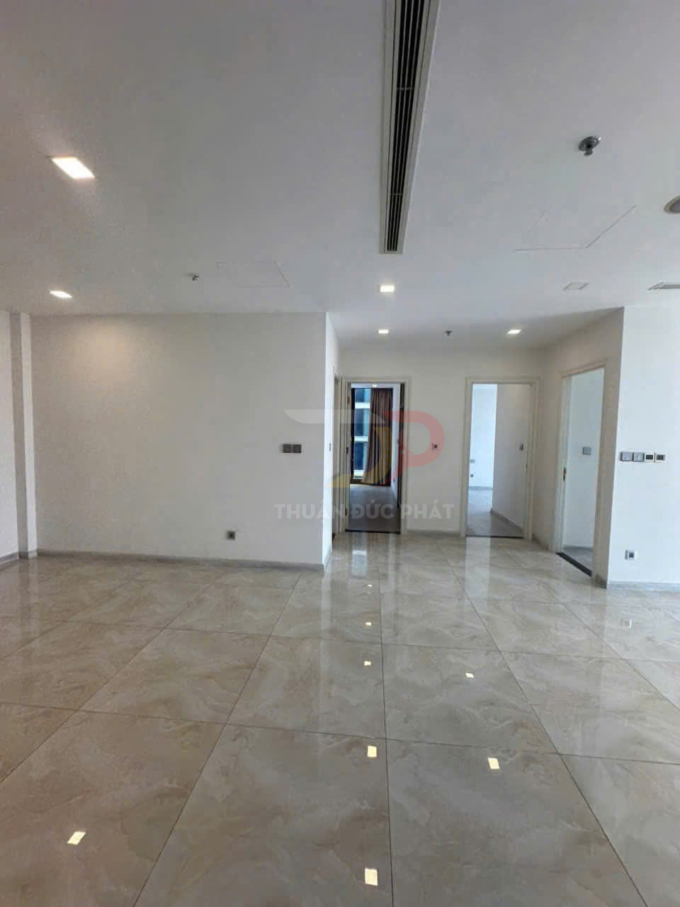 Căn hộ trống lát gạch bóng, trần thạch cao đèn âm trần, cửa dẫn vào các phòng ngủ