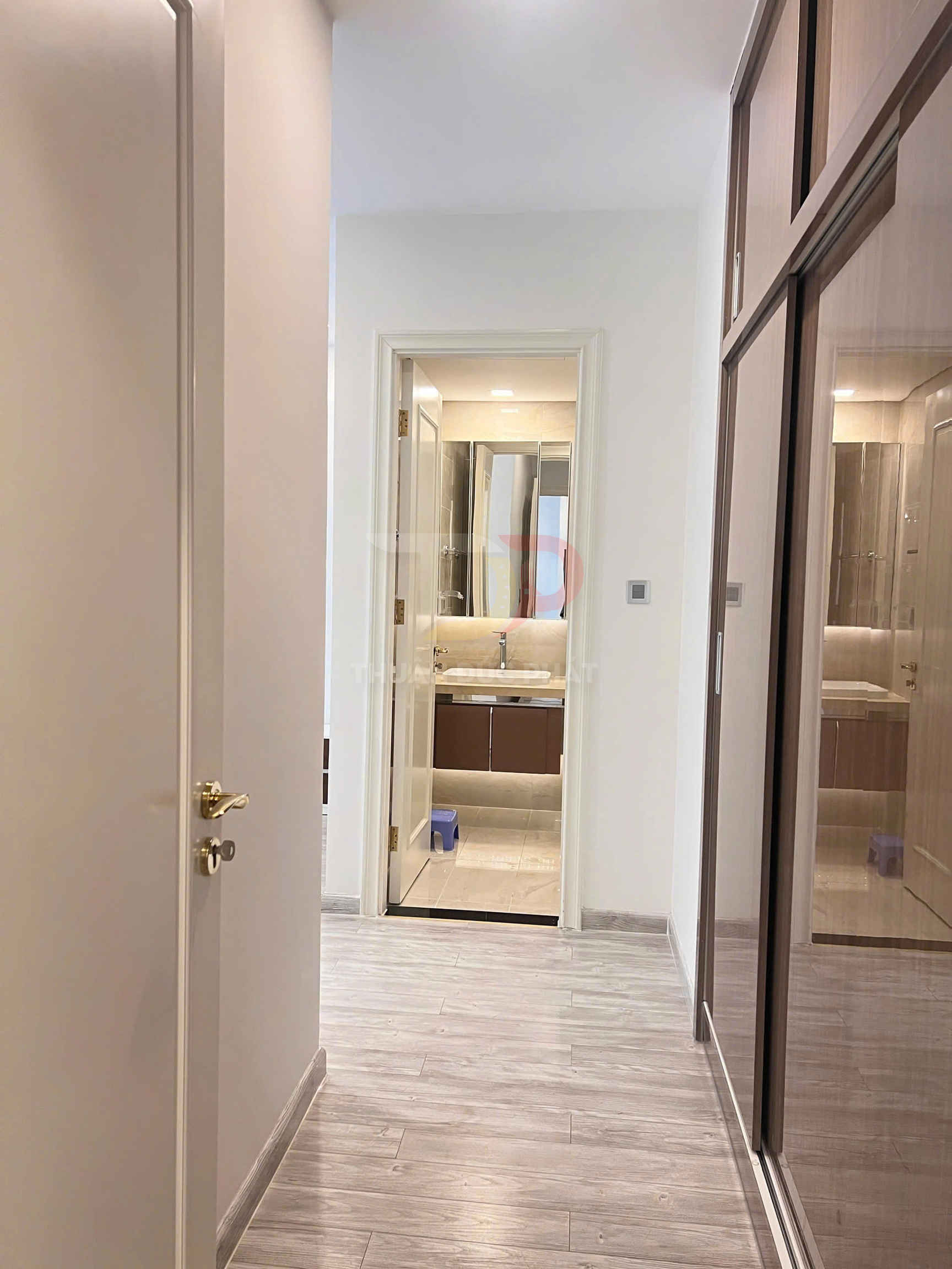 Hành lang căn hộ lát sàn gỗ dẫn vào phòng tắm hiện đại với tủ lavabo và gương lớn