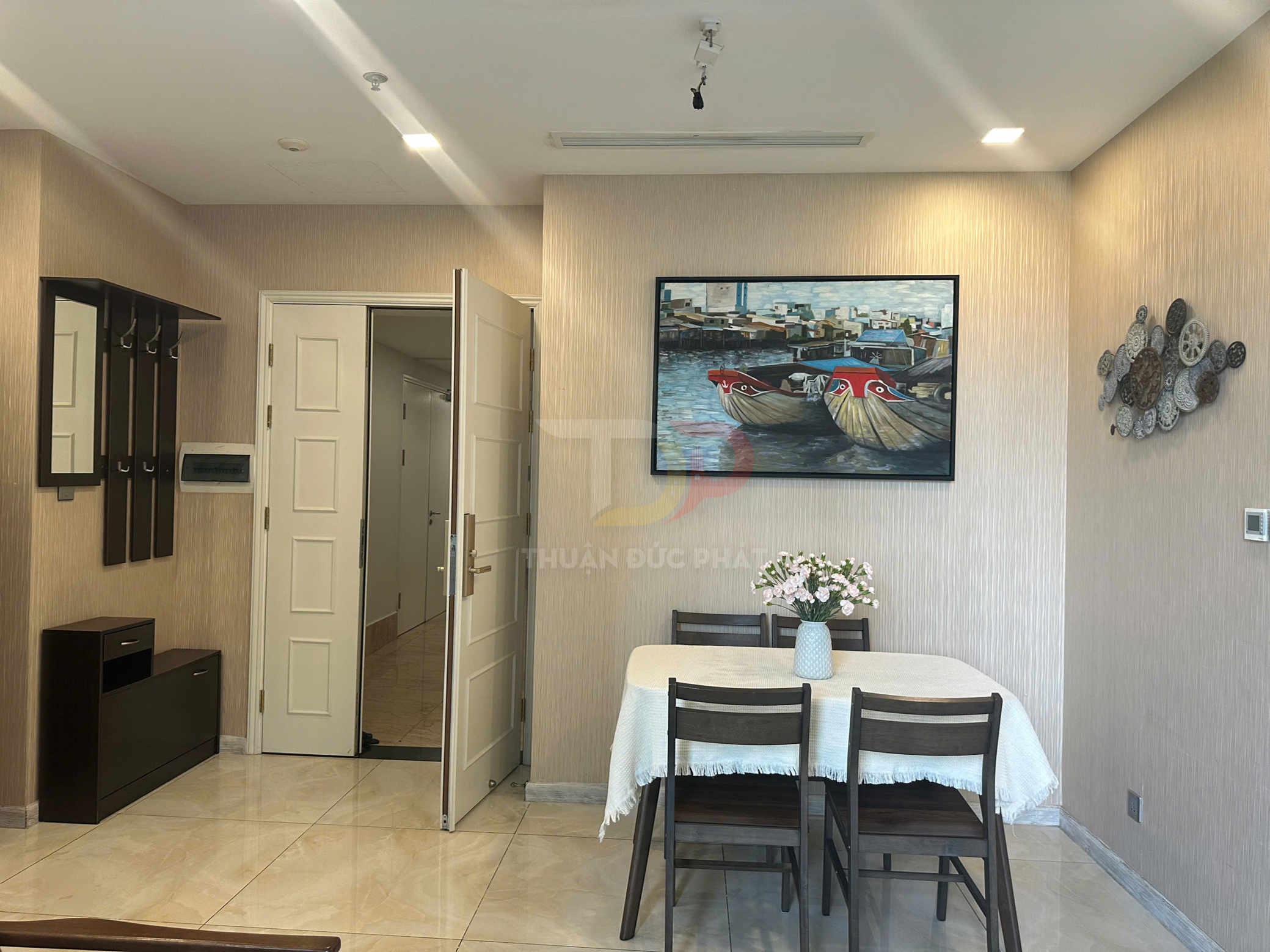 Bộ bàn ăn gỗ 4 ghế phủ khăn trắng trong phòng ăn chung cư trang trí tranh thuyền và bình hoa