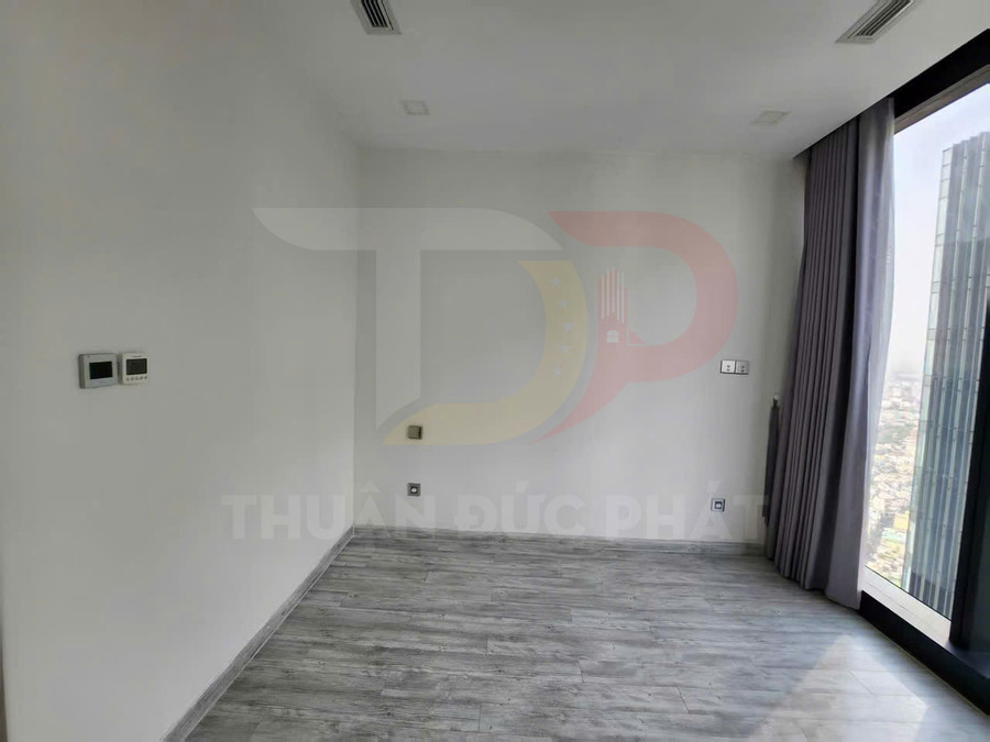 Phòng trống lát sàn gỗ màu xám, tường trắng, cửa kính lớn có rèm nhìn ra thành phố