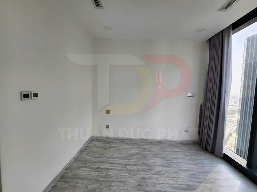 Phòng trống lát sàn gỗ màu xám, tường trắng, cửa kính lớn với rèm xám nhìn ra thành phố