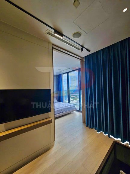 Phòng ngủ chung cư hiện đại với giường cạnh cửa kính lớn và rèm xanh, sàn gỗ sáng màu