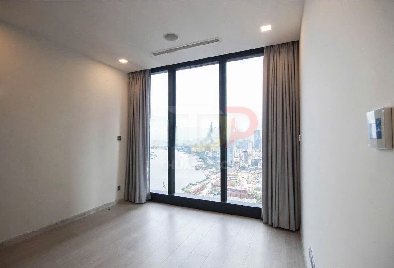 Phòng ngủ trống với cửa kính lớn sát sàn, rèm xám và view toàn cảnh sông cùng thành phố