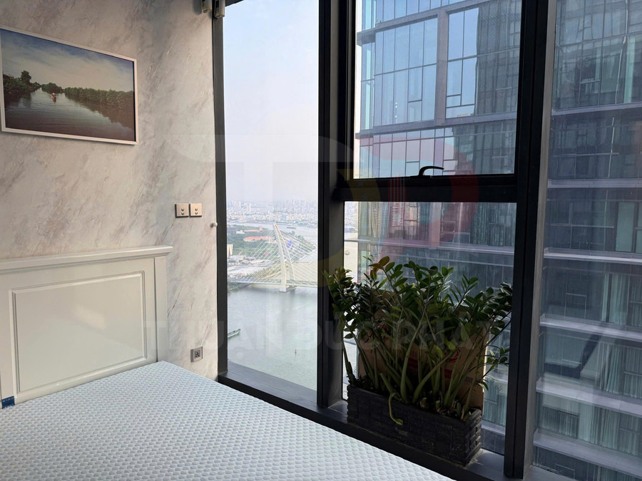 Phòng ngủ chung cư với giường cạnh cửa sổ lớn, chậu cây xanh và view sông cùng cầu hiện đại bên ngoài